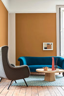 Little Greene Middle Buff 122 verf op muur in stijlvolle woonkamer met blauw fluwelen bank en houten vloer.